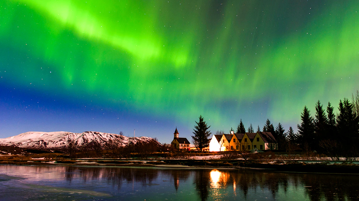 Northern Lights over snowy landscape and houses in Iceland.