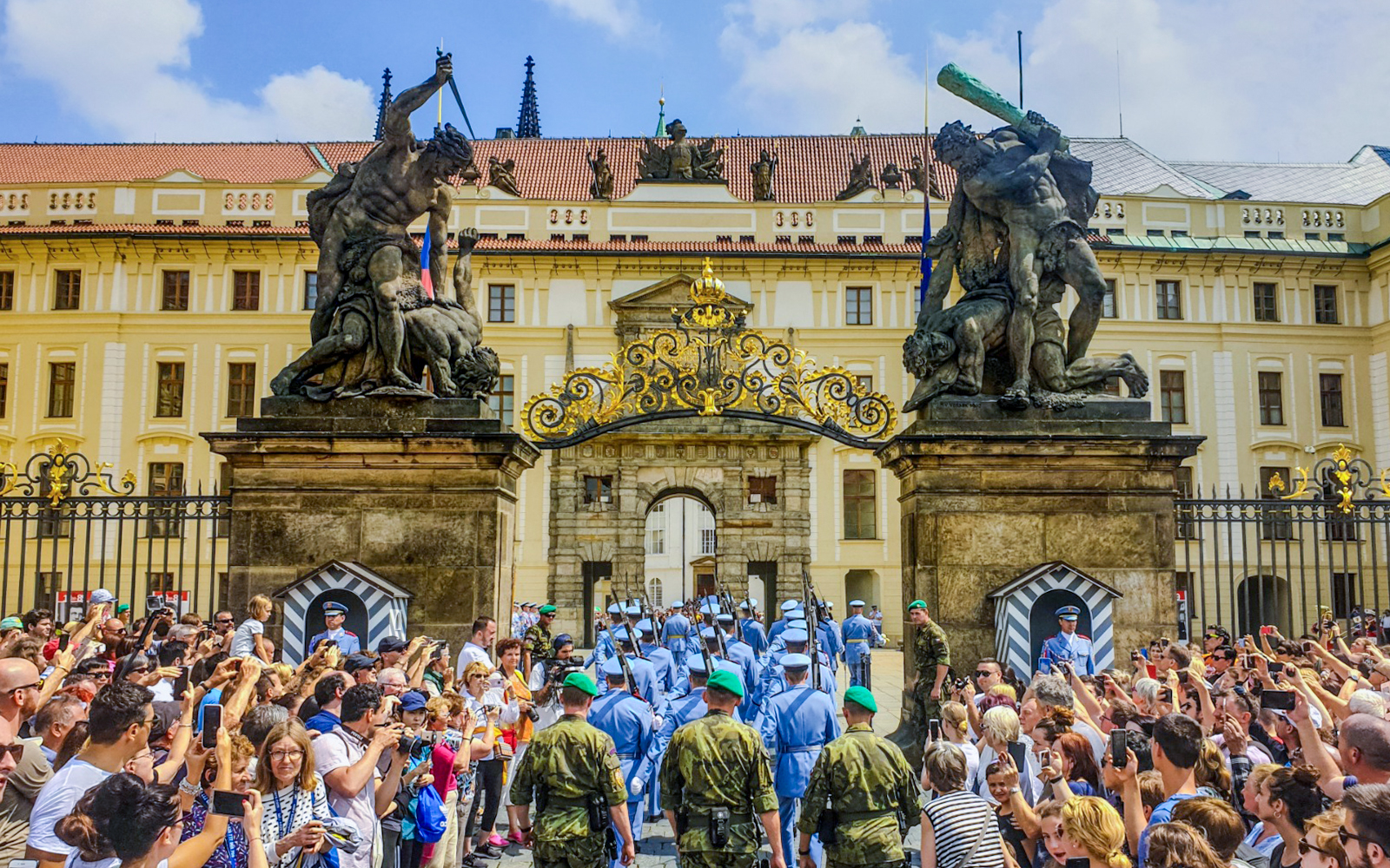 Ceremony at Prague Castle entrance with guards and crowd gathered.