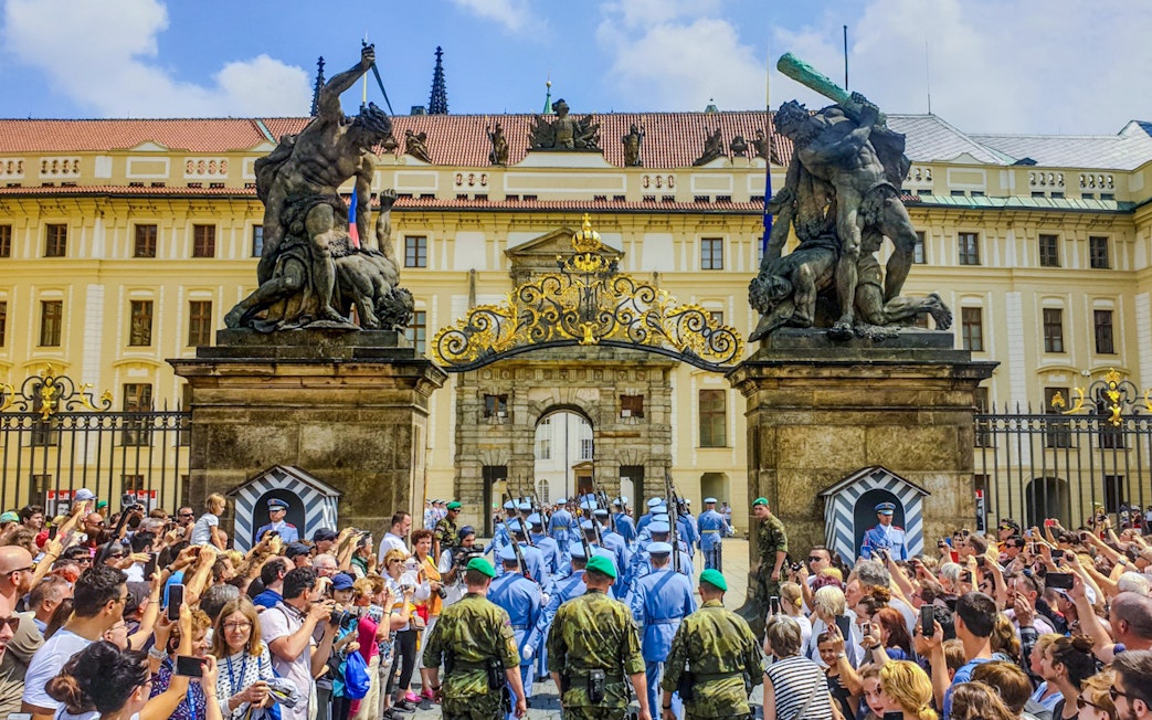 Ceremony at Prague Castle entrance with guards and crowd gathered.