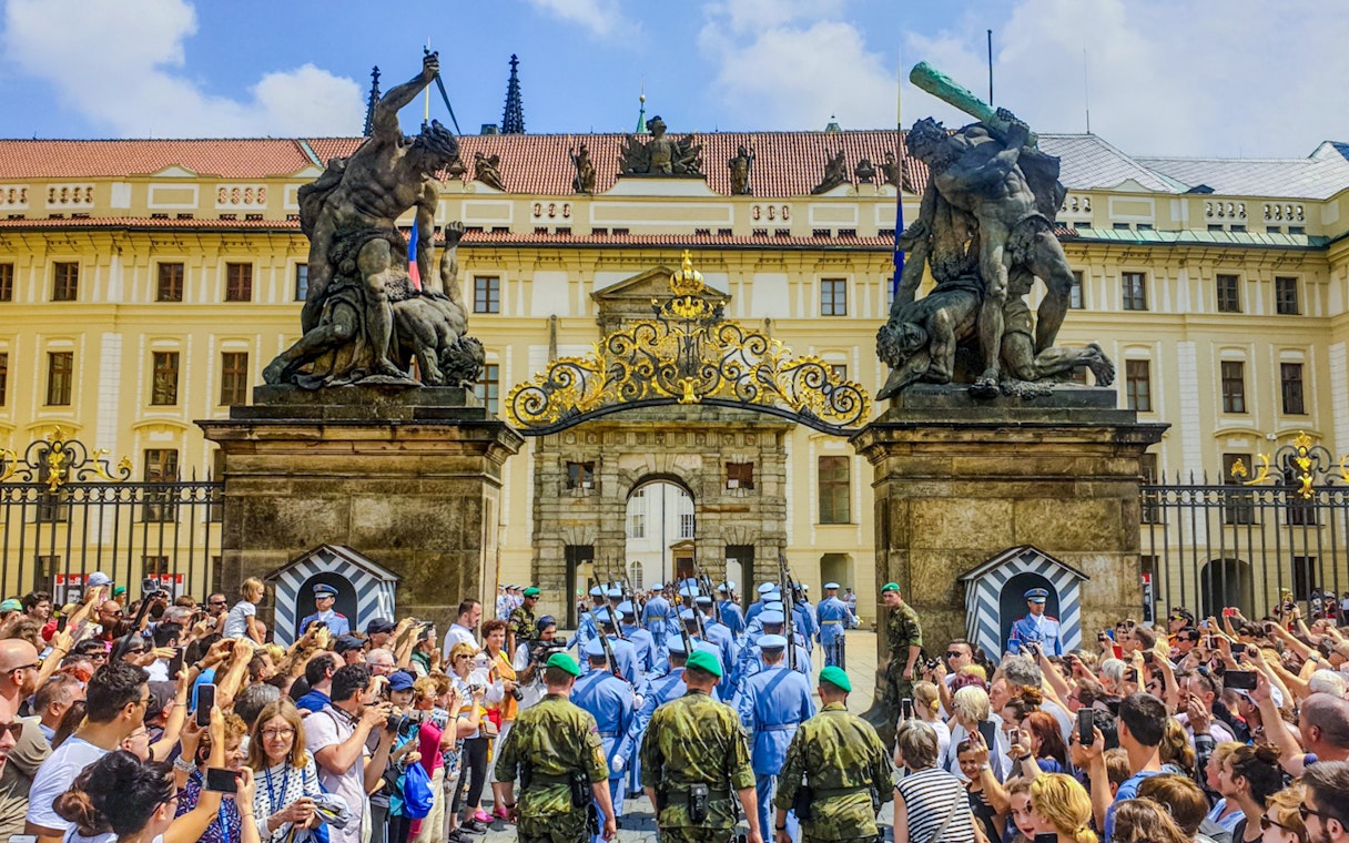 Ceremony at Prague Castle entrance with guards and crowd gathered.