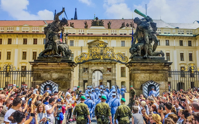 Ceremony at Prague Castle entrance with guards and crowd gathered.