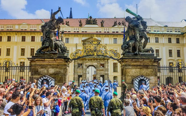 Ceremony at Prague Castle entrance with guards and crowd gathered.