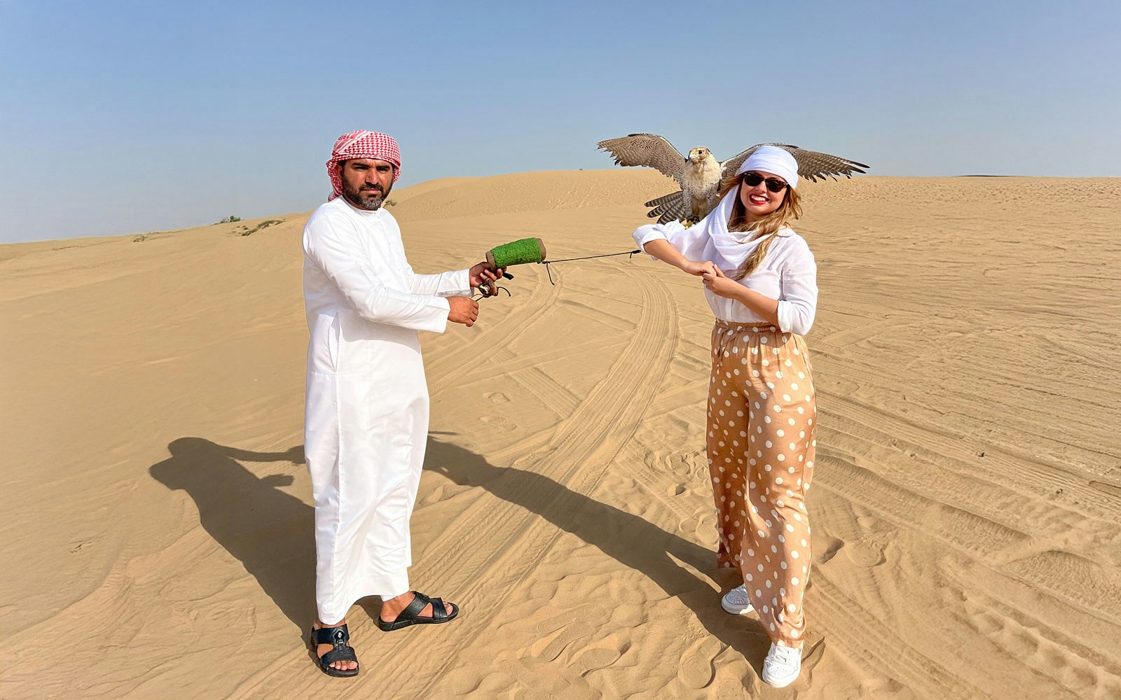 Falconer and tourist with falcon in Dubai desert show.