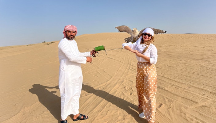 Falconer and tourist with falcon in Dubai desert show.