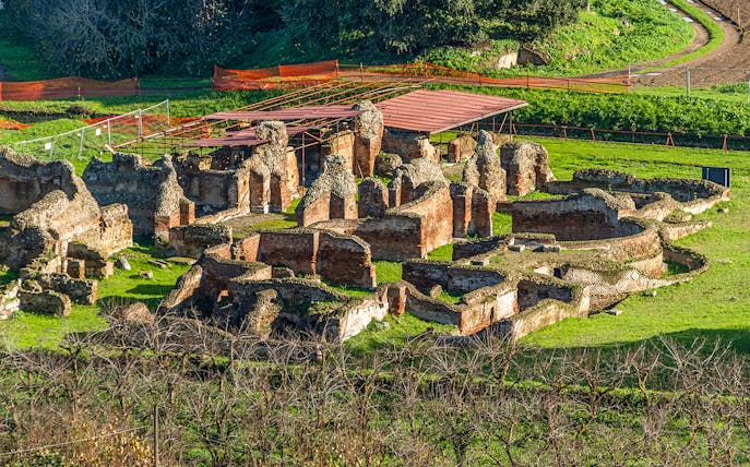 Ancient ruins at the Archaeological Park of Cumae, Italy, surrounded by greenery.