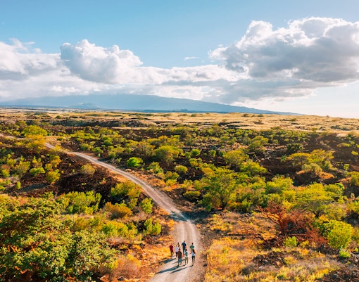 Group walking on a trail through Maunakea's scenic landscape during the Summit & Stars Giveback Experience.
