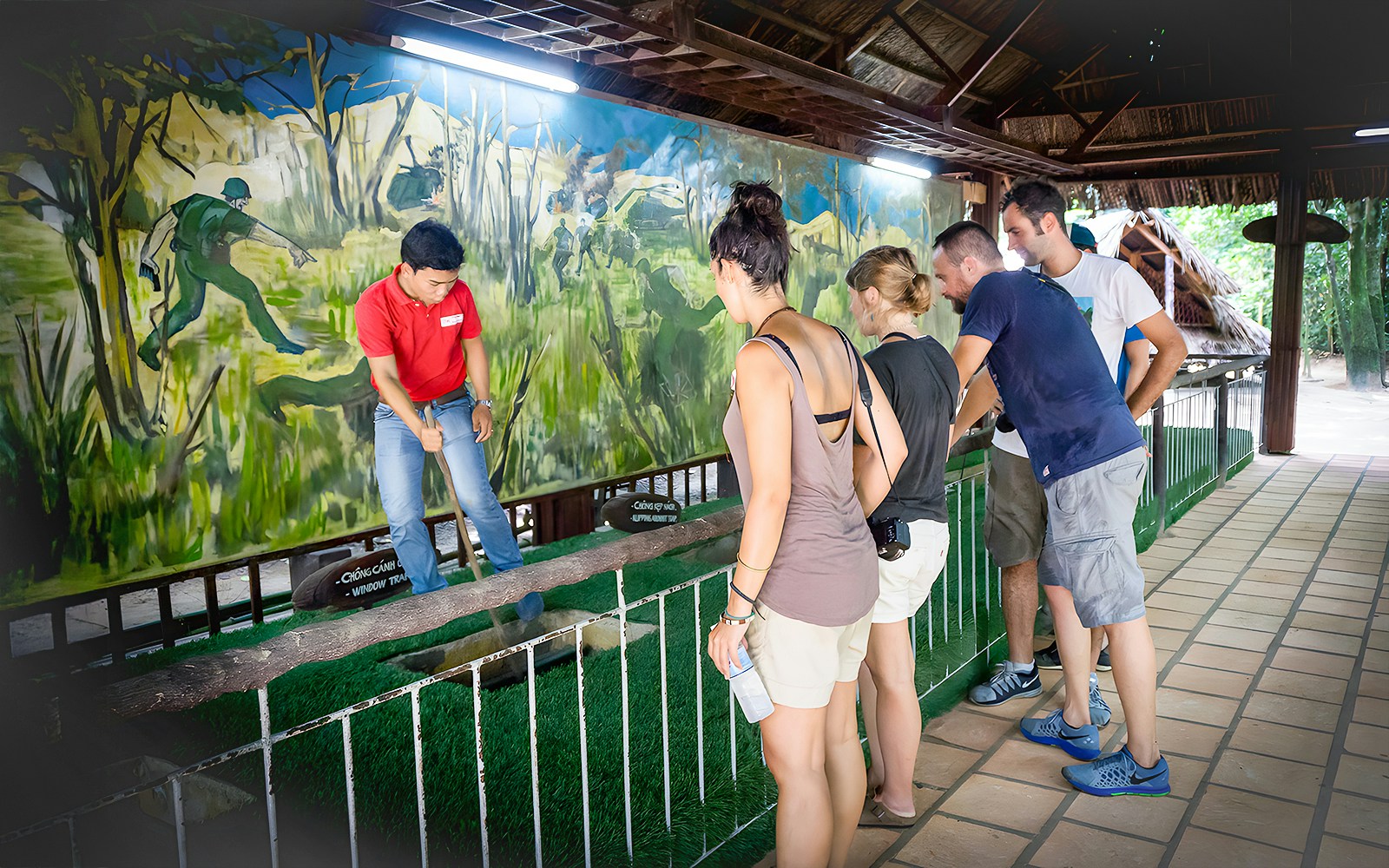 Guide demonstrating booby trap mechanism to tourists at Cu Chi Tunnel, Vietnam.