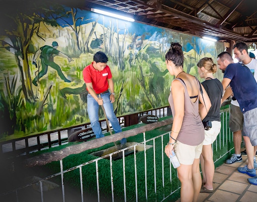 Guide demonstrating booby trap mechanism to tourists at Cu Chi Tunnel, Vietnam.