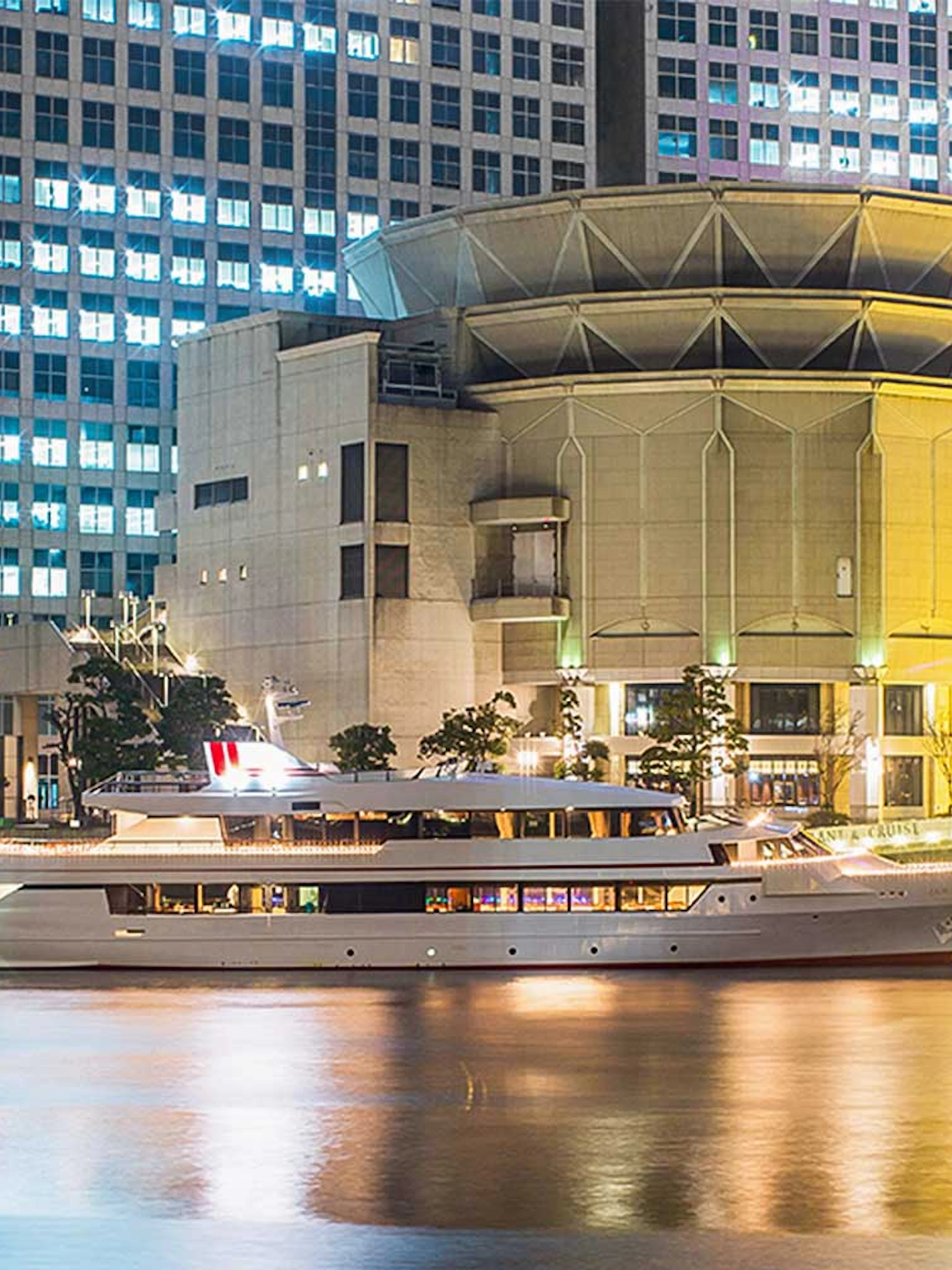 Cruise ship docked at night in front of illuminated buildings in Tokyo.