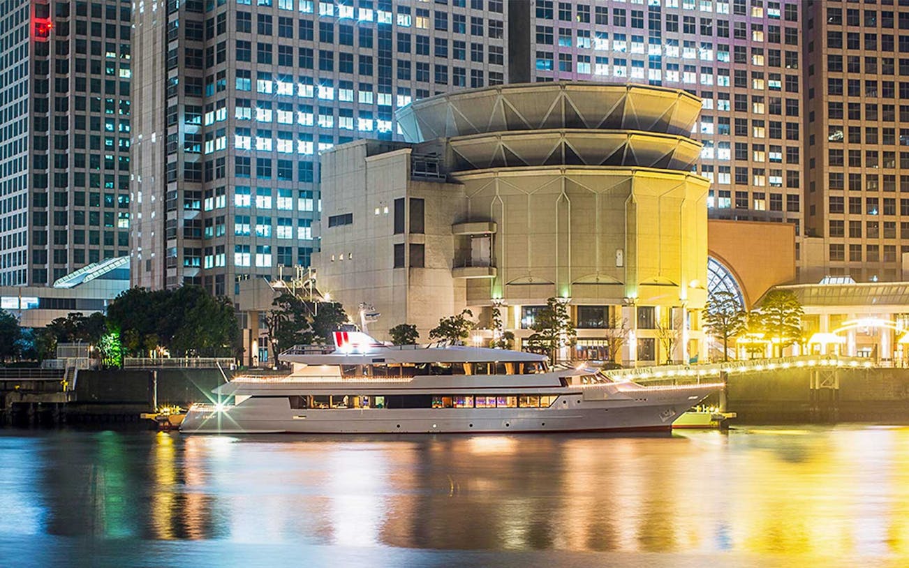 Cruise ship docked at night in front of illuminated buildings in Tokyo.