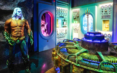 Statue of Aquaman in front of a control room with colorful lights and machinery.