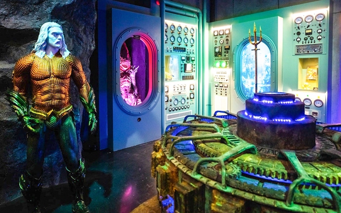 Statue of Aquaman in front of a control room with colorful lights and machinery.