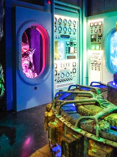 Statue of Aquaman in front of a control room with colorful lights and machinery.