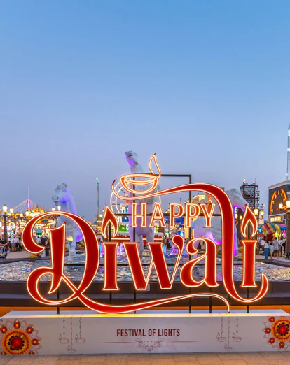 Global Village Diwali sign with festive lights and visitors in Dubai.