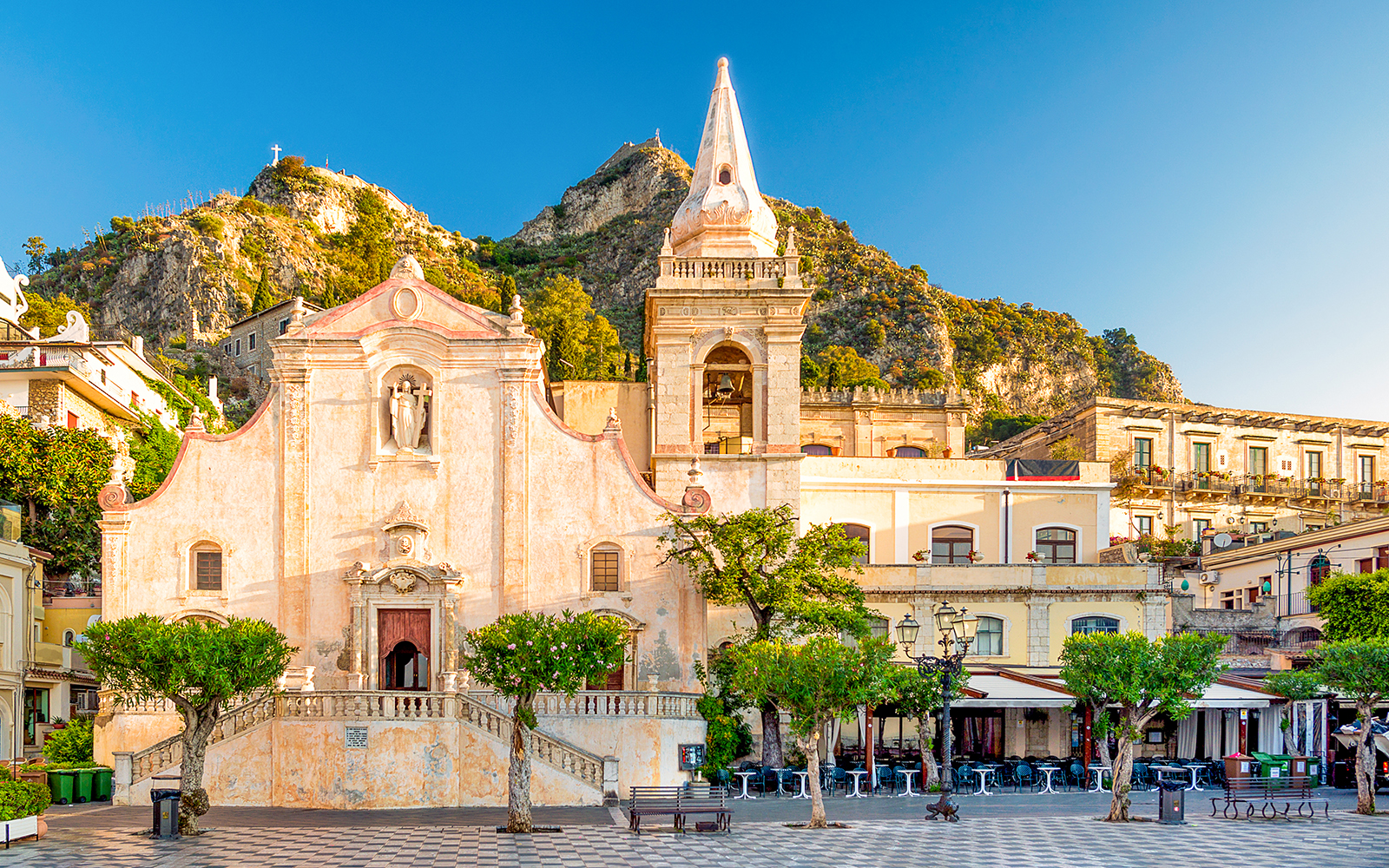 Taormina's Piazza IX Aprile with historic church and mountain backdrop.