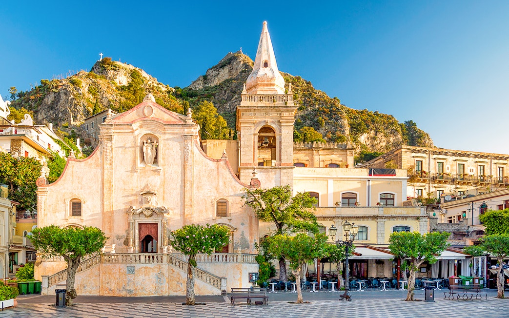 Taormina's Piazza IX Aprile with historic church and mountain backdrop.