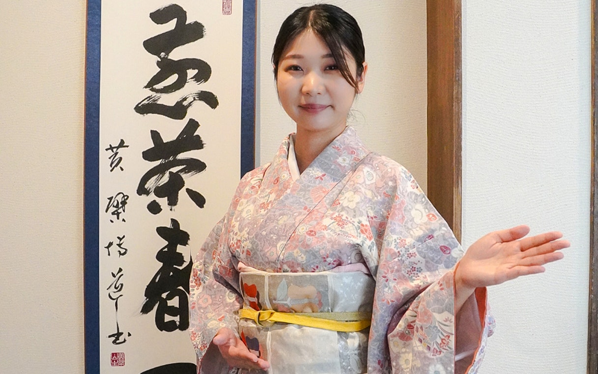 Woman in kimono beside Japanese calligraphy scroll in Japan.