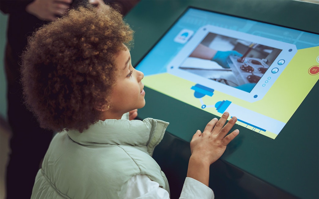 Child interacting with touchscreen at The Chocolate Story Museum exhibit.