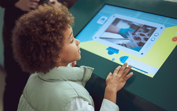 Child interacting with touchscreen at The Chocolate Story Museum exhibit.