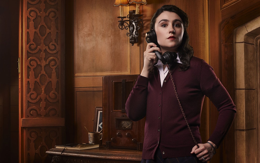 Person holding a vintage telephone in a wood-paneled room, related to The Mousetrap.