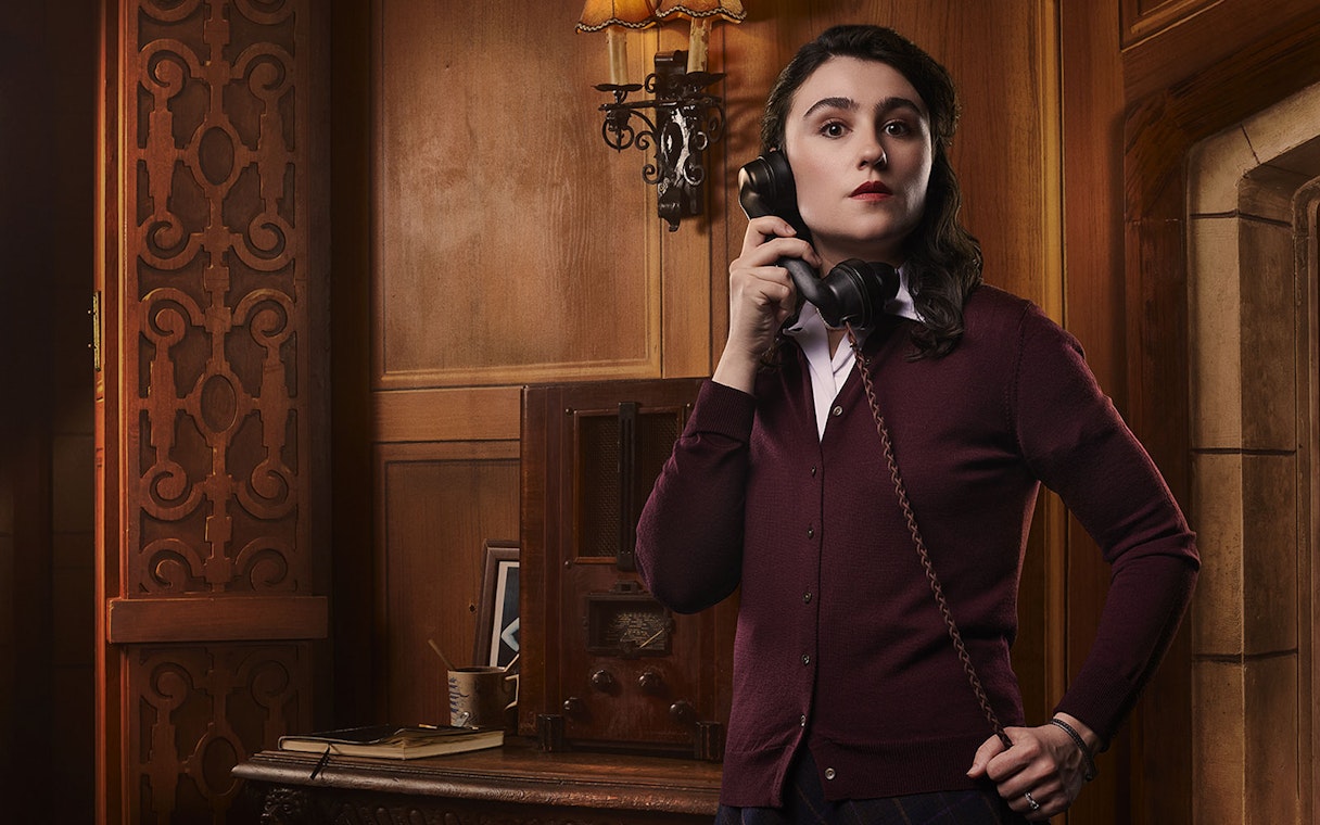 Person holding a vintage telephone in a wood-paneled room, related to The Mousetrap.