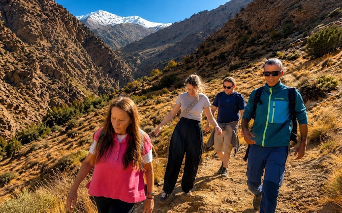 Hikers exploring Ourika Valley in Atlas Mountains, Marrakech, with snow-capped peaks in the background.