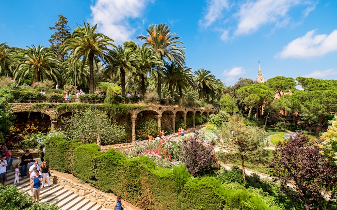 Park Guell's Walk of the Palm Trees with stone arches and lush gardens in Barcelona.