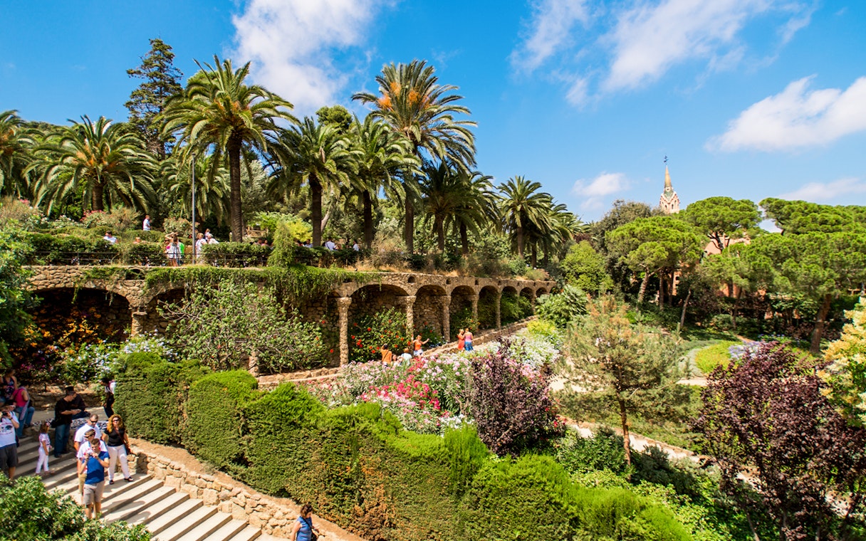 Park Guell's Walk of the Palm Trees with stone arches and lush gardens in Barcelona.