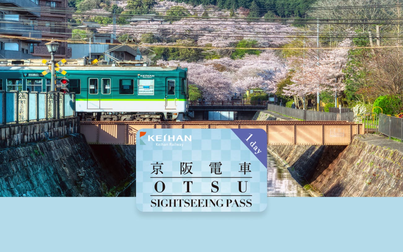 Keihan Railway train passing cherry blossoms in Otsu with sightseeing pass in foreground.