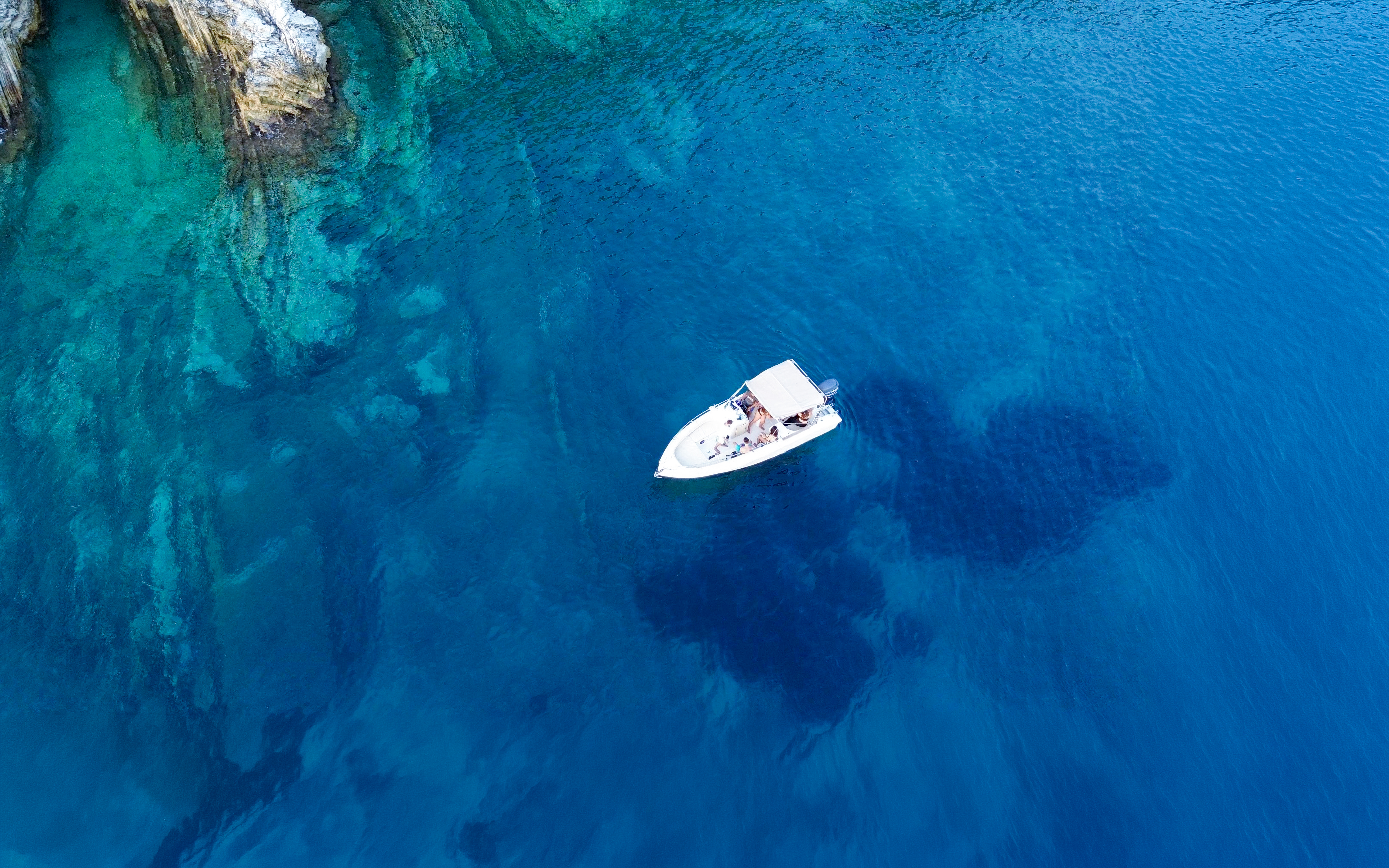 Boat exploring clear waters near rocky cliffs on Ionian Coast tour.