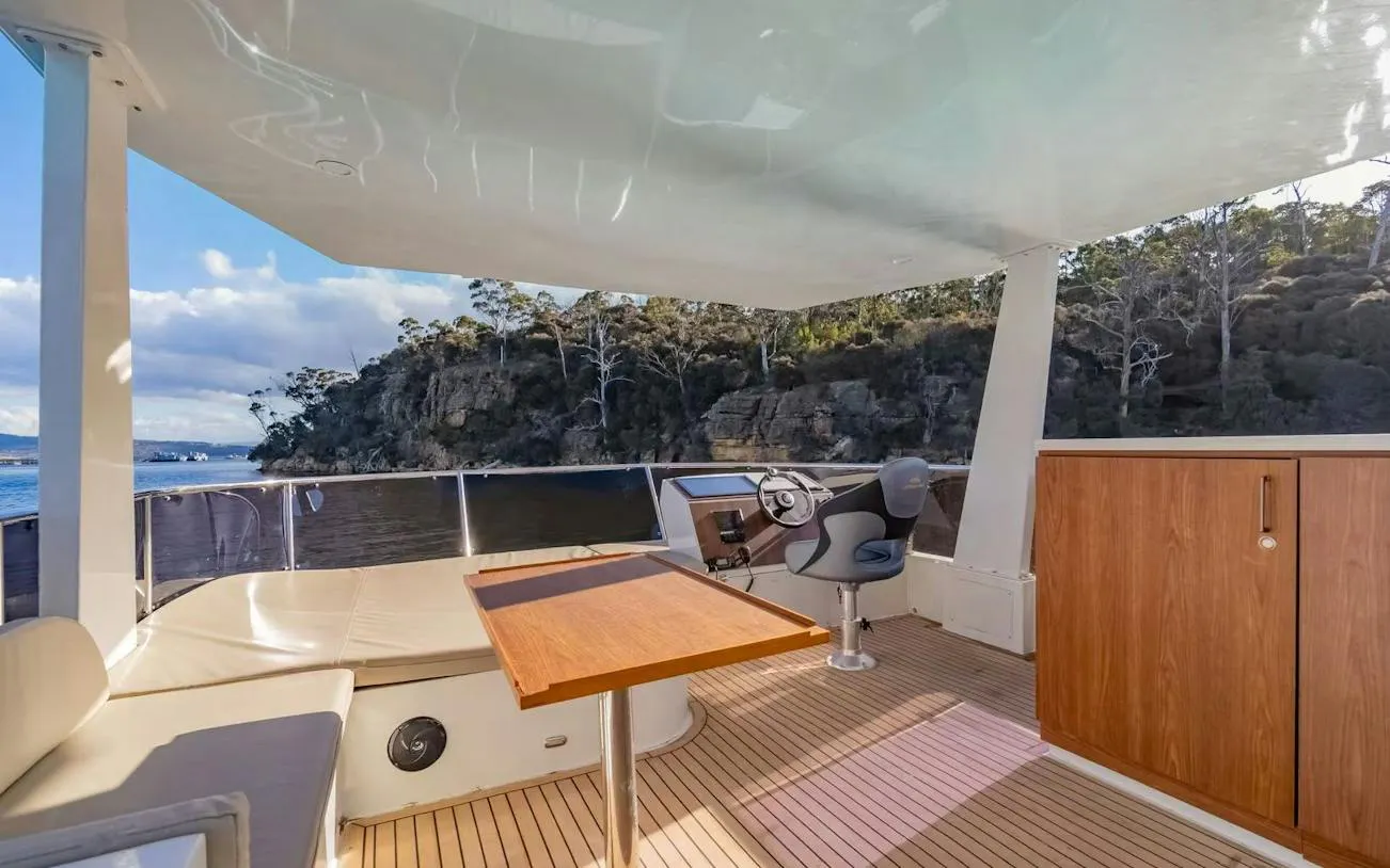 Cruise boat deck with seating and steering area, scenic view of Hobart coastline.
