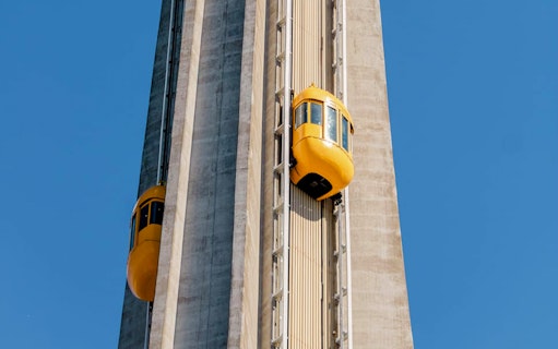 Yellow-Bug elevators ascending Skylon Tower against blue sky.