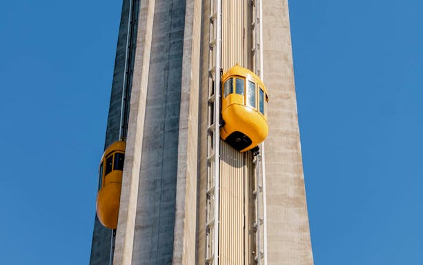 Yellow-Bug elevators ascending Skylon Tower against blue sky.