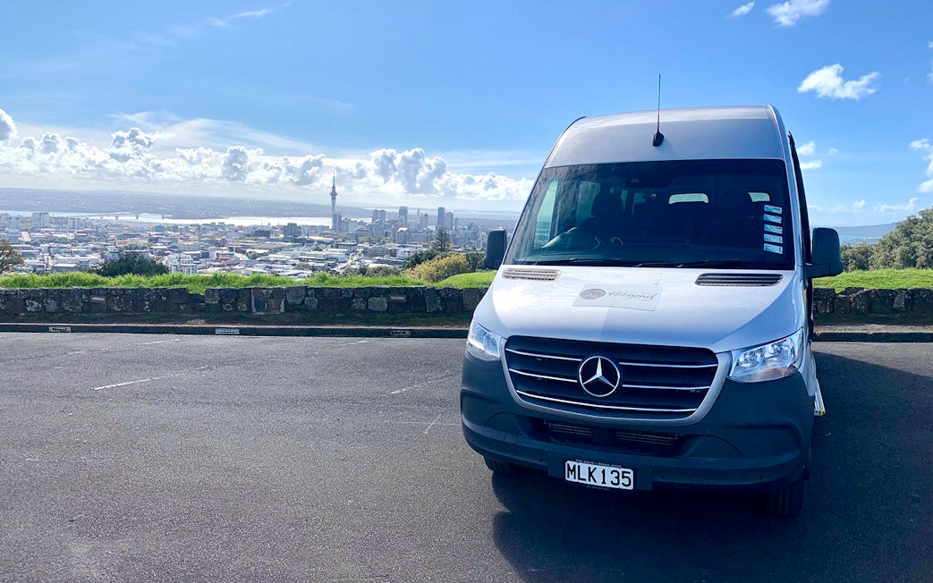 Shuttle van in Auckland with city skyline, used for transfers to Hobbiton and Rotorua tours.