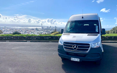 Shuttle van in Auckland with city skyline, used for transfers to Hobbiton and Rotorua tours.