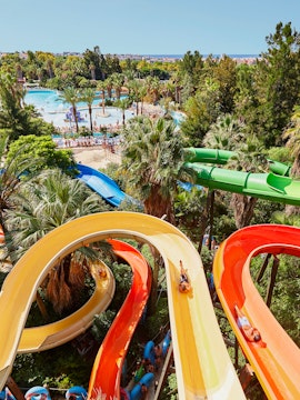 Aerial view of Caribe Aquatic Park with colorful water slides and pools surrounded by lush greenery.