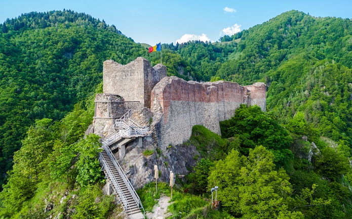 Poenari Fortress in Romania surrounded by lush green hills and a staircase leading up to the ruins.