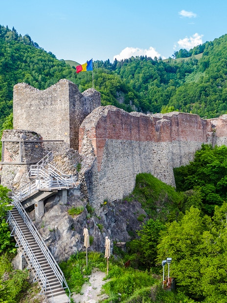 Poenari Fortress in Romania surrounded by lush green hills and a staircase leading up to the ruins.