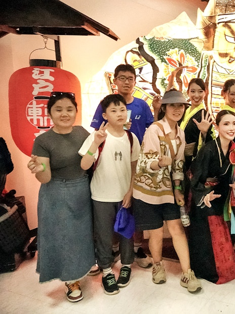 Dancers in traditional attire posing with tourists in front of a vibrant festival lantern.