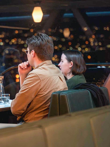 Dinner guests enjoying a meal on an Aurora Boreal cruise with city lights in the background.