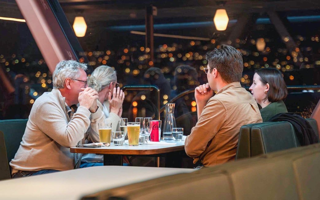 Group enjoying drinks on a Northern Lights cruise with city lights in the background.