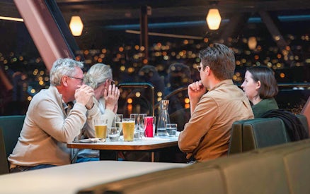 Group enjoying drinks on a Northern Lights cruise with city lights in the background.