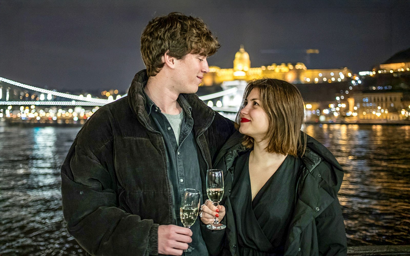 Guests enjoying drinks on a Danube sightseeing cruise with Budapest landmarks in the background.