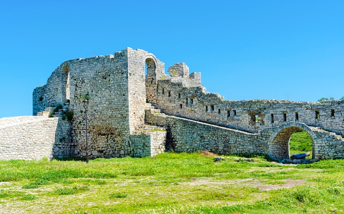 Berat Castle stone walls and archway under a clear blue sky in Albania.