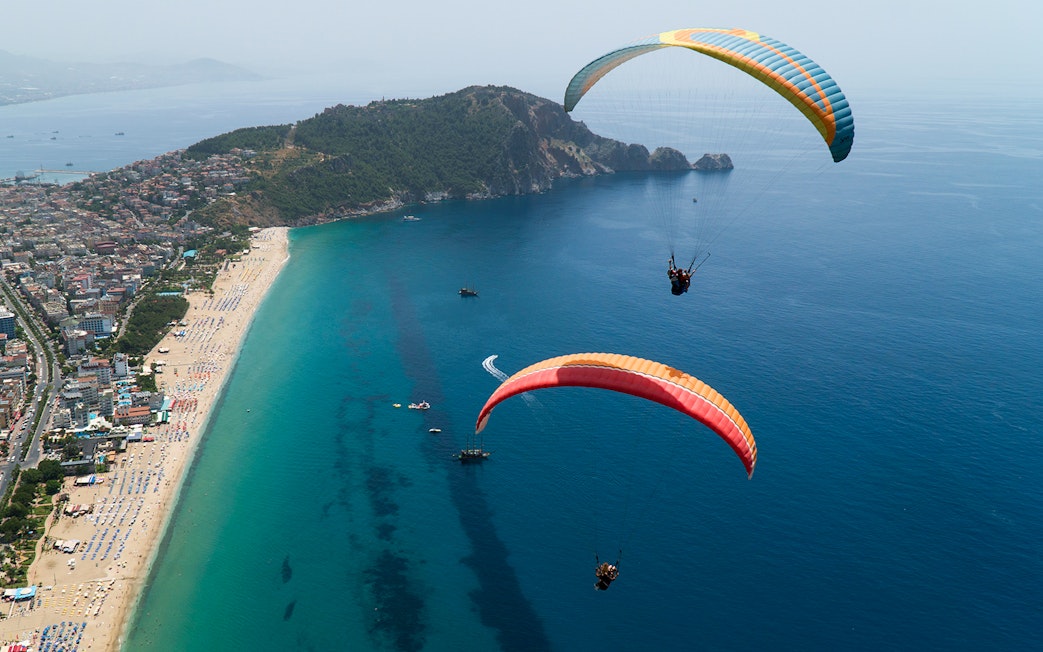 Paragliders soaring over Alanya coastline with city and sea view.