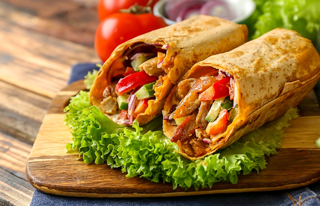 Chicken shawarma wraps with vegetables on a wooden board.