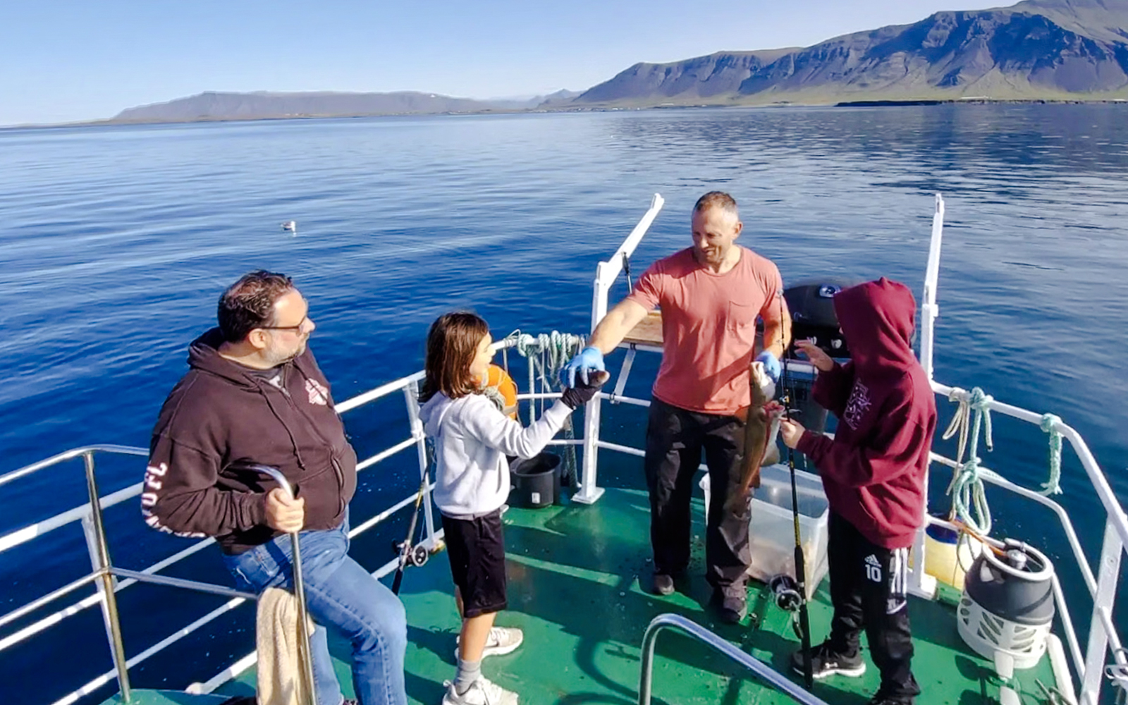 Guests fishing on a boat during Reykjavík Sea Angling Gourmet Tour with mountains in the background.