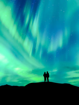 Silhouette of a couple watching the aurora borealis in a clear night sky.