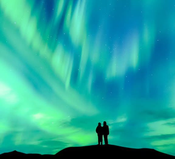 Silhouette of a couple watching the aurora borealis in a clear night sky.
