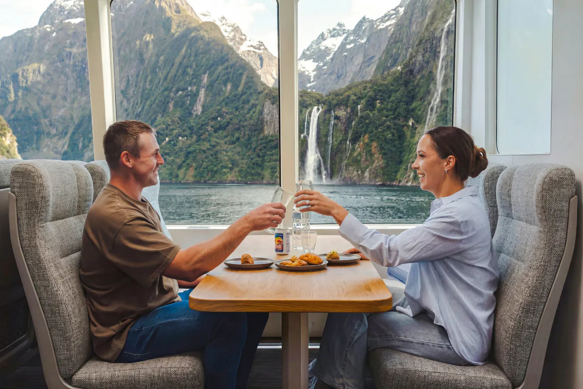 Couple enjoying a meal with a view of Milford Sound waterfall on a VIP cruise from Queenstown.